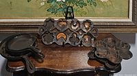 Six vintage cast iron cookware pieces displayed including cookie/cake mold, heart and star baking pan skillet, muffin pans, and two cast iron skillets on a wooden surface with decorative background.