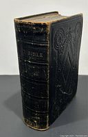 Front cover of the 1869 Holy Bible showing black leather with embossed patterns and gold title on spine; edges show age wear.