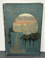 Front cover of the 1891 book Scottish Pictures, showing blue cloth cover with gilt and black text and illustrations including a circular Scottish landscape and building.