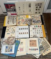 Full view of the collection including multiple binders, loose sheets, and bags of stamps spread over a floor surface.