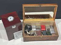 Image showing the carved wooden box with multiple Zippo lighters inside and the wood humidor with hygrometer beside it.