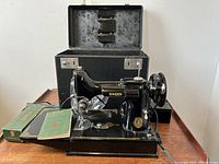 Singer 221 Featherweight machine on its baseplate with open carrying case, green accessory box and manuals visible on wooden table
