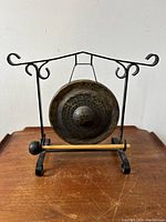 Front view of the brass dinner gong suspended in wrought iron stand with wood mallet in front.