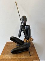Angled view of seated Nubian terracotta figurine holding a spear on wooden surface.