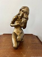 Front view of the statue showing the nude kneeling lady with detailed hair and figure.