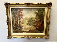 Full view of framed landscape oil painting showing autumn trees and river.