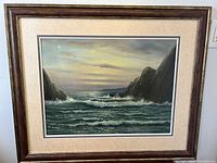 Full view of the framed seascape oil painting depicting rocky cliffs with waves crashing between them under a cloudy sky.