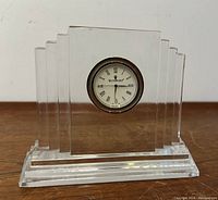 Front view of clear Waterford crystal podium clock with circular clock face and Roman numeral markings seen on wooden surface.