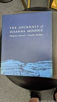 Blue slipcase with title 'The Journals of Susanna Moodie' with author names Margaret Atwood, Charles Pachter, featuring a blue landscape illustration.