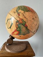 Side view showing the illuminated globe mounted on a wooden base, revealing antique style map and lighting mechanism with electrical cord.
