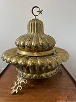 Front side view of brass brazier burner showing fluted rounded shape with vent holes and crescent moon and star finial on top.