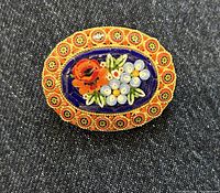 Close-up photo showing detailed micro mosaic floral pattern with red, white, and green colors on blue background, set in ornate goldtone oval frame with red and yellow accents.