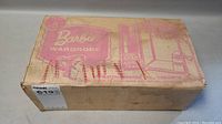 Worn cardboard box with Barbie Wardrobe label in pink and significant stains and creases on box surface