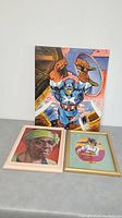 Photo of three art pieces including Captain America painting and two framed portraits.
