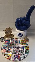 Photo showing all five items including the large Captain America comic themed clock, ship wheel clock, two smaller clocks, and large blue Toronto Maple Leafs foam hand glove.
