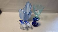 Four items: light blue plastic item labeled 593, transparent blue glass goblet, blue glass dolphin figurine, and dolphin paperweight sculpture.