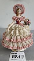Front angle of the Royal Doulton Lady in Frilly Dress figurine showing details of the multi-layered pink and cream dress, bonnet, and floral basket.