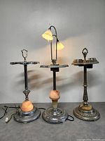 Front view of three vintage Art Deco items showing two ashtrays and one electric lamp with floral-shaped light shades.