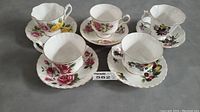 Lot of five vintage fine bone china cups and matching saucers with diverse floral patterns and gold trim under natural light