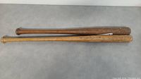Two vintage wooden baseball bats lying flat showing length and color difference, Wilson bat darker and longer, Winner bat lighter and shorter.