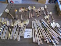 Full set of flatware items arranged on table with visible patterned handles and some tarnishing.