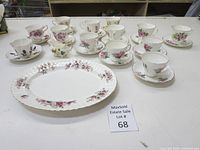 Full view of bone china tea cups, saucers, large serving platter, and sauce boat on white surface.