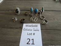 Photo showing assortment of 11 rings on a wooden surface behind a MaxSold Estate Sale Lot Card