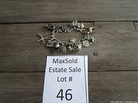 Silver-tone charm bracelet arranged with charms visible on wood surface with lot number card.