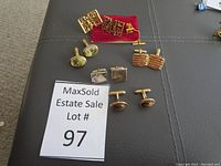 Set of assorted cufflinks and one tie pin arranged on a dark surface, showing the variety of designs and materials.