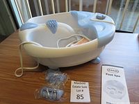 Full view of the Dr. Scholl's Foot Spa basin in white and blue plastic with power cord and instruction manual nearby on a wooden table.