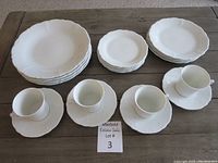 Full set showing 4 cups on saucers, and stacks of plates in three sizes, arranged on a wooden table.