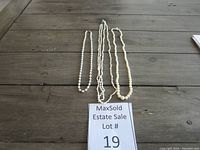 Overview of three pearl necklaces arranged side by side on a wooden surface with an estate sale label showing lot number 19.