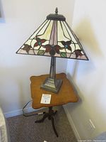 Full view of the lamp showing stained glass shade with floral design on a small wooden table.