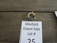 Photo of the vintage 12K gold filled brooch with a circular shape, multicolor rhinestones in clear, blue, green, and red, and a gold bow at the top, displayed on wooden surface.