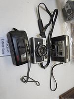 Photo of three vintage film cameras: Ricoh AF-77, Ricoh 500 G, and Keystone 825 EF arranged on a white surface.