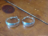 Pair of rounded 925 silver hoop earrings laid flat on wooden surface to show overall shape and reflectiveness.