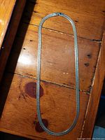 Full-length view of braided silver necklace laid flat on wooden surface