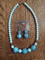 Full view of necklace laid flat with matching earring pair attached to plastic card, showing bead details and gold-tone clasp.