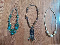 Photo of three handcrafted necklaces laid flat on wood floor, showcasing color and bead details.