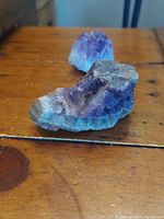 Two natural amethyst geodes displayed on a wooden surface, showing purple crystalline structures and natural rough bases.