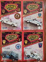 Four packaged Road Champs State Police Series 1/43 scale diecast cars showing front view with police badges and vehicle models.