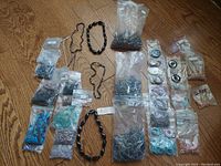 Multiple bags of unfinished drilled stones and jade raw jewelry parts, spread on wooden surface.