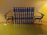 Pair of vintage brass antelope bookends holding a row of classic books between them, showcasing their use and size.