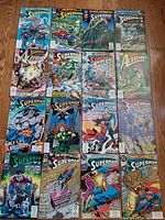 Collection of sixteen vintage Superman comic books laid out on wooden floor showing various covers from 1990s.