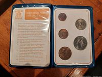 Coins displayed in original Royal Mint presentation folder showing obverse and reverse sides of coins along with historical and design information.