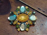 Close-up photo of the vintage lock pin brooch showing the oval and round semi-precious stones in multiple colors and yellow rhinestones.