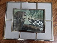 Full shot of framed Sue Coleman 'Face to Face' raccoon art print showing metal frame and fabric inset on wood surface.