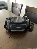 Closed Ambico camera bag showing front and side pockets, adjustable shoulder strap and logo on front pocket.