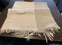 Image of a Crate and Barrel blanket laid on a table showing the woven texture in beige and cream blocks with fringed edges.