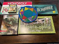 Seven board games including Monopoly, Scrabble, Alpaca-opoly, Chinese Checkers, Dungeons & Dragons Starter Set, and a small puzzle, shown together on a table.